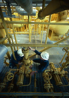 Two men working on pipes inside a facility