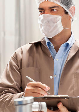 Man wearing a mask and hair cap writing on a clipboard while looking at something to his right