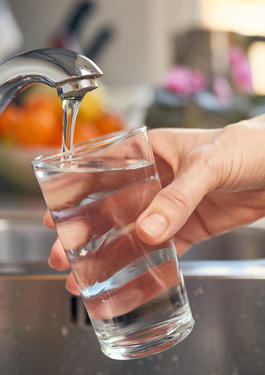 clear drinking glass being held under a faucet with running water