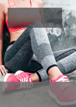 person wearing sports bra and leggings sitting against a grey wall