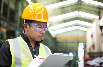 Man wearing hard hat and safety goggles holding clipboard