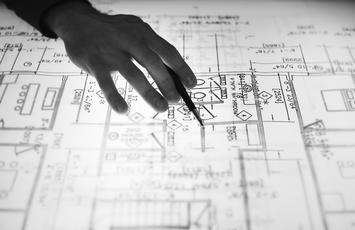 Plans layout on lightened table, human hand with pencil panning over the plans paper