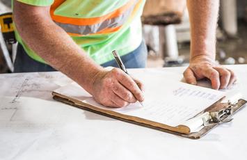 Man writing on a pad of paper attached to a clipboard in a work surface
