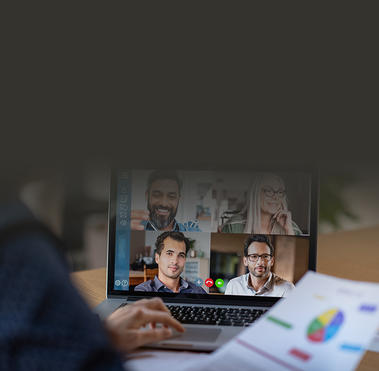 Woman sitting at desk holding a paper at an open laptop with four people on video call