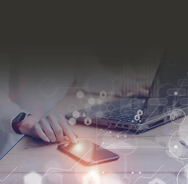  Person sitting at their laptop touching a cell phone sitting at their desk